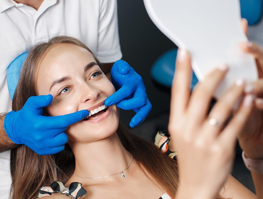 Dentista le muestra en un espejo cómo han quedado los dientes de su paciente tras el blanqueamiento dental.