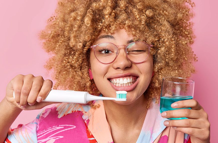 Mujer con cepillo dental eléctrico y un vaso con enjuague bucal.
