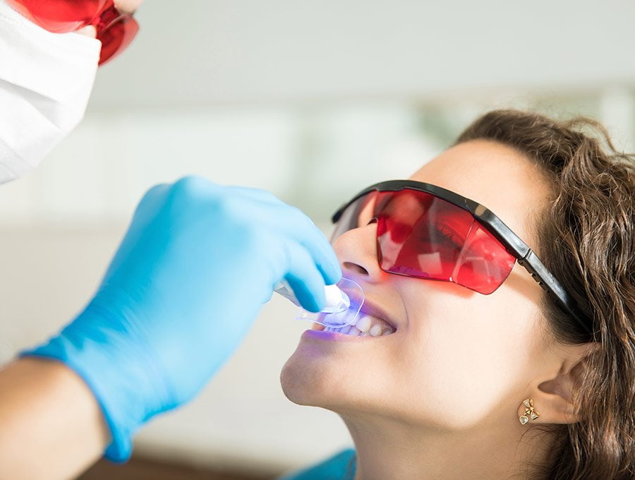 Dentista aplicando un blanqueamiento dental por láser sobre su paciente.