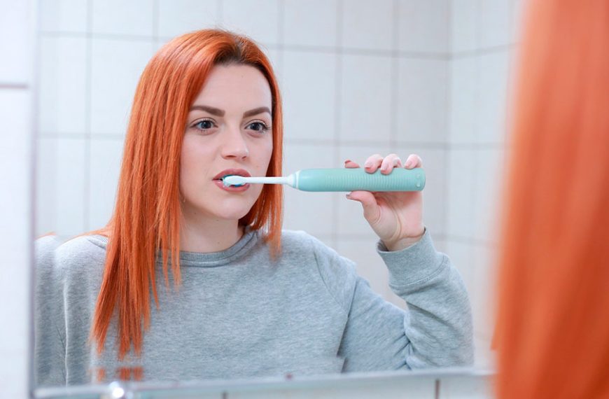 Chica de cabello pelirrojo se cepilla los dientes delante del espejo.