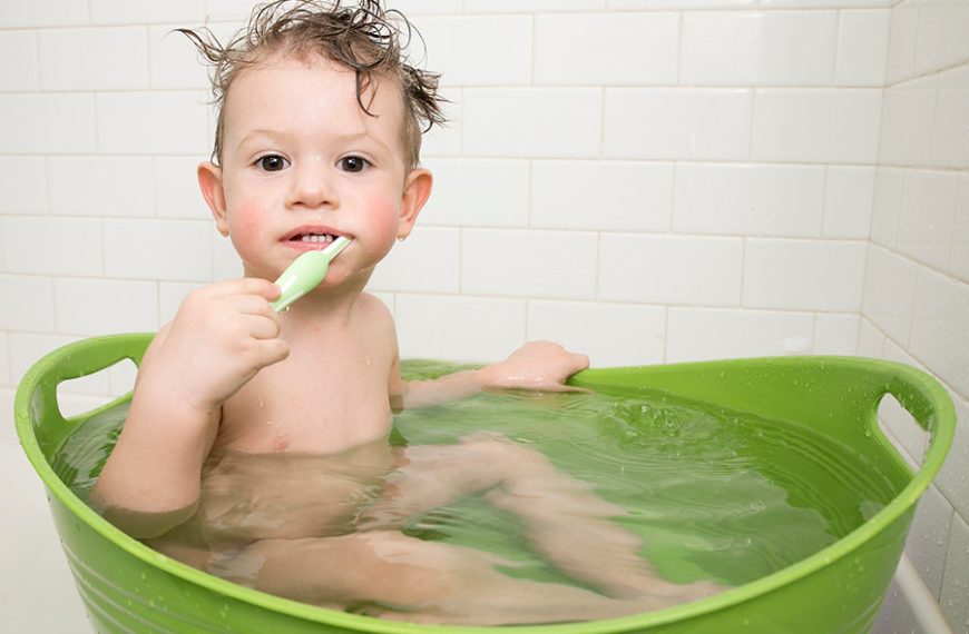 El niño pequeño se cepilla los dientes dentro del barreño mientras se baña.
