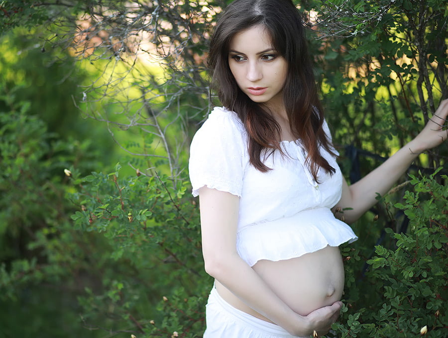 Mujer embarazada junto a los árboles del jardín. Se distrae por el dolor de muelas.